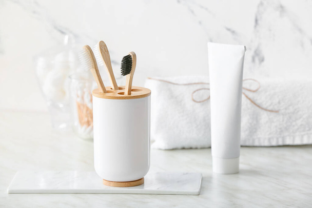 Holder with wooden toothbrushes and toothpaste on table in bathroom - Photo, Image