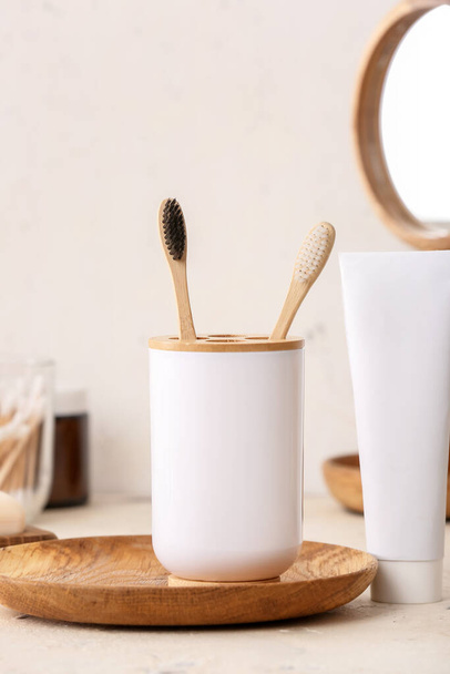 Soporte con cepillos de dientes de madera y pasta de dientes en la mesa en el baño - Foto, Imagen