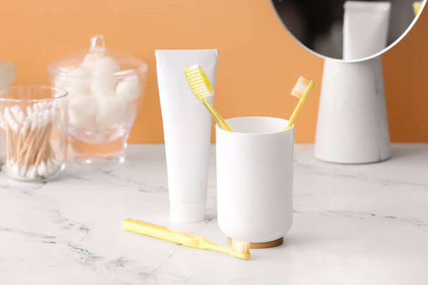 Тримач з зубними щітками і зубною пастою на столі у ванній
 - Фото, зображення