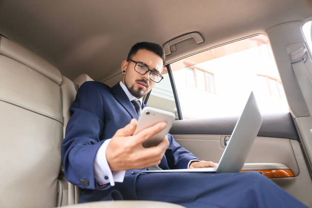 Exitoso hombre de negocios con portátil y teléfono móvil en coche moderno - Foto, Imagen