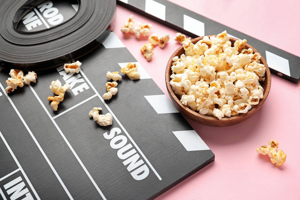 Bowl of popcorn, film reel and clapperboard on color background - Zdjęcie, obraz