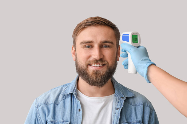 Człowiek i ręka z termometrem na podczerwień na tle światła. Epidemia koronawirusa - Zdjęcie, obraz