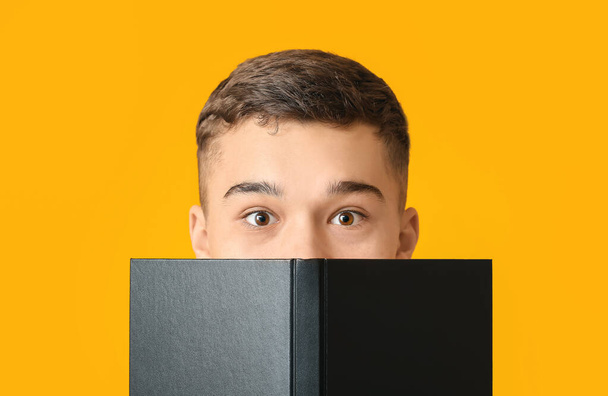 Surprised teenage boy with book on color background - Foto, Imagen