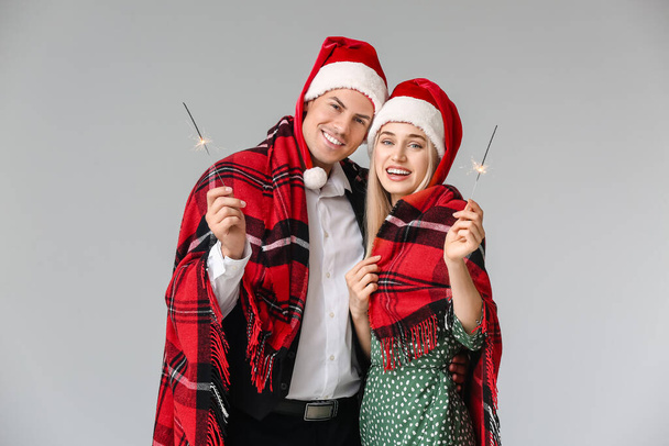 Happy young couple with Christmas sparklers on grey background - Photo, Image