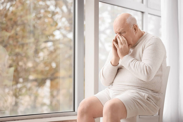 Sad senior man near window in clinic. Prostate cancer awareness concept - Fotó, kép