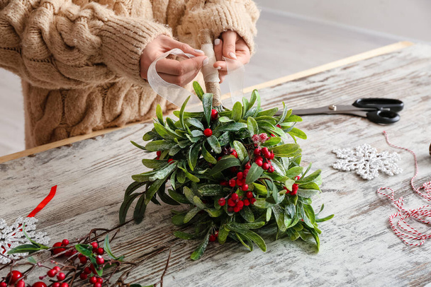 Woman making composition with mistletoe branches on table - Photo, Image