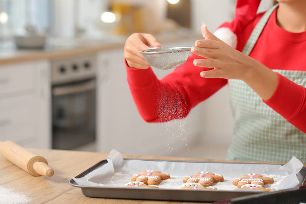 Young woman baking tasty gingerbread cookies in kitchen on Christmas eve - Photo, Image