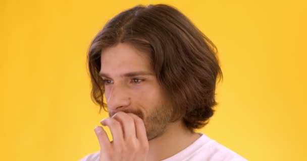 Close up portrait of young timid man feeling confused, looking uncertainty at camera, covering mouth, orange background - Footage, Video