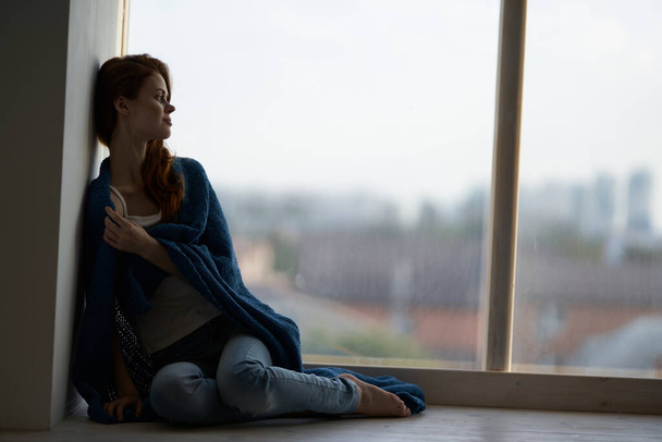 Frau sitzt auf Fensterbank mit Decke bedeckt - Foto, Bild