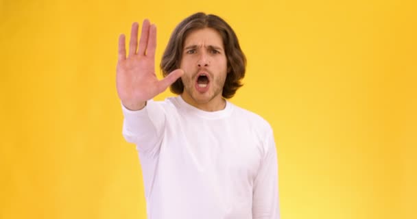 Joven hombre serio mostrando gesto de stop y cruzando las manos, sacudiendo la cabeza en el rechazo, fondo naranja estudio - Metraje, vídeo