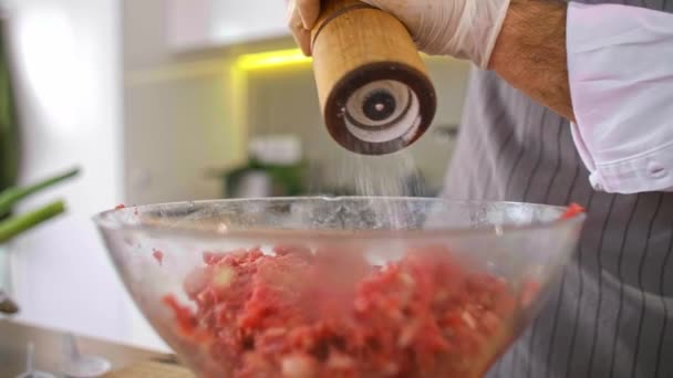 肉、玉ねぎ、ベーコンと透明なガラスのボウルにスパイスを追加シェフ,作業面の側に野菜がある間,ベーコンのスライス,スパイスや小さなキッチン用品.. - 映像、動画