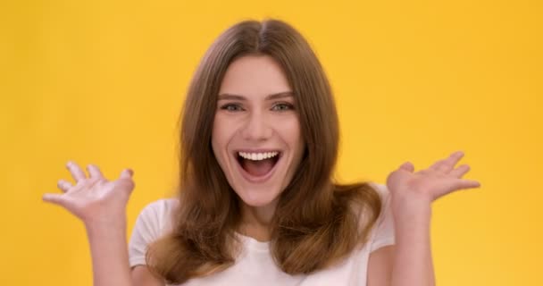 Young happy surprised woman shouting in amazement and delight, touching her cheeks, yellow studio background - Footage, Video