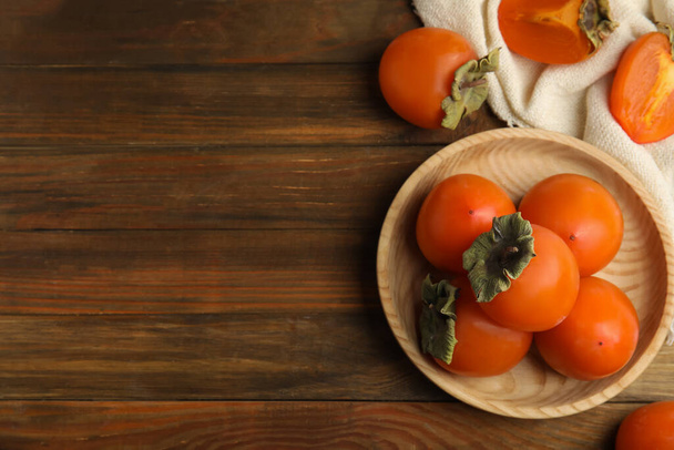 Tasty ripe persimmons on wooden table, flat lay. Space for text - Foto, imagen