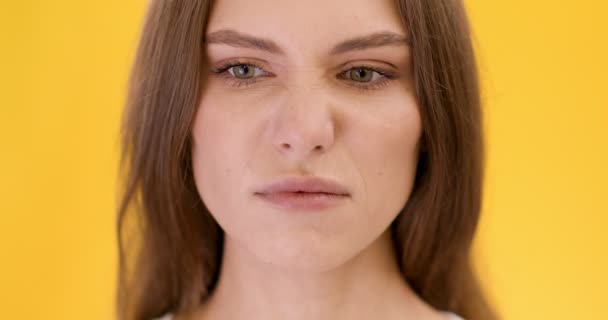 Close up portrait of young woman smelling something awful, closing nose, frowning in displeasure, orange background - Footage, Video