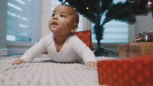 Schattige pasgeboren baby die een buikje heeft omringd door cadeautjes. Eerste baby kerstmis - Foto, afbeelding