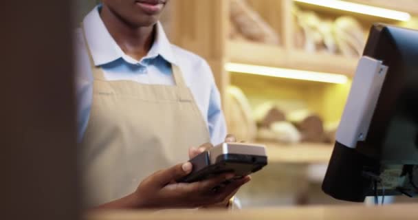Pastanede satış yapan Afrikalı Amerikalı kadın satıcıya ödeme yapmak için cihaz kullanarak yaklaşın. Beyaz müşteriler fırından alırken kredi kartıyla ödeme yapıyorlar. İş konsepti - Video, Çekim