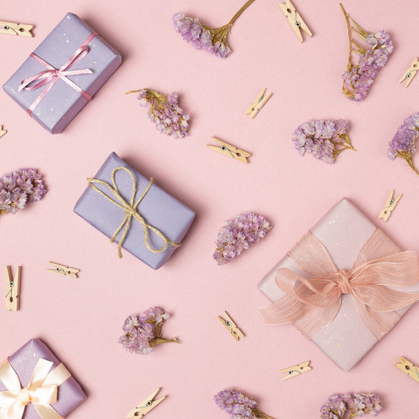 Cajas de regalo de color rosa pastel y púrpura con flores secas y clips de madera sobre fondo rosa. plano, vista superior - Foto, imagen