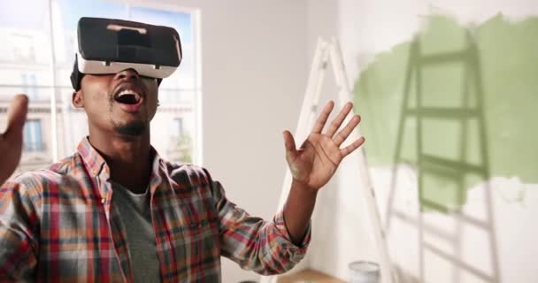 Κοντινό πλάνο του Αφροαμερικανού νεαρού εντυπωσιασμένου άνδρα στέκεται στο δωμάτιο φορώντας γυαλιά εικονικής πραγματικότητας και κοιτάζοντας το νέο επανασχεδιασμένο ανακαινισμένο διαμέρισμα χρησιμοποιώντας σύγχρονες καινοτομίες. Τεχνολογία εικονικής πραγματικότητας - Πλάνα, βίντεο