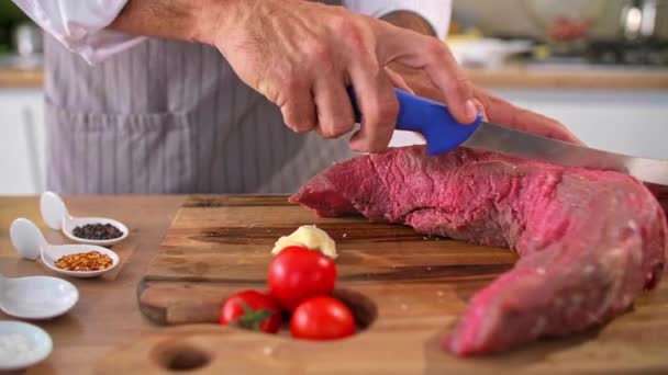 Keittiömestarin kädestä lähikuva, jossa liha leikataan ohuiksi paloiksi veitsellä. Erilaisia mausteita ja vihanneksia voidaan nähdä ympäri. - Materiaali, video