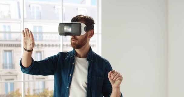 Κοντινό πλάνο του όμορφου νεαρού Καυκάσιου epairman που φοράει γυαλιά VR, κυλιέται με τα χέρια στον αέρα χρησιμοποιώντας σύγχρονες τεχνολογίες καινοτομίας επιλέγοντας το σχεδιασμό του σπιτιού. Σχέδιο επισκευής και ανακαίνισης. Εικονική πραγματικότητα - Πλάνα, βίντεο