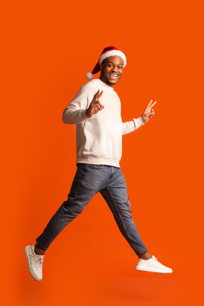 Εορταστική χαρά. Αφρικανός στο Santa Hat Διασκεδάζοντας πάνω από πορτοκαλί φόντο - Φωτογραφία, εικόνα