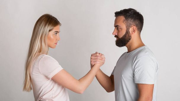 Jonge man en meisje kijken serieus naar elkaar en knijpen hun handen in arm worstelen - Foto, afbeelding