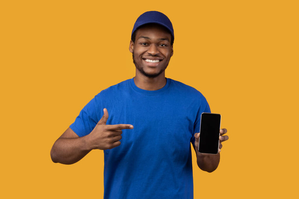 Black delivery man holding smartphone with blank screen for mockup - Foto, afbeelding