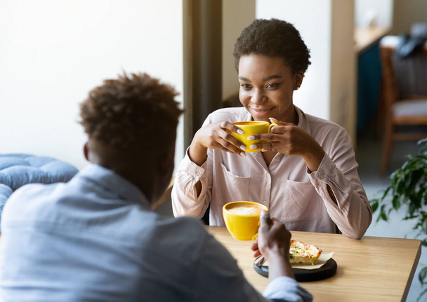 Hombre negro guapo con su novia disfrutando de un café aromático y tener una conversación amistosa en la cafetería de la ciudad - Foto, imagen