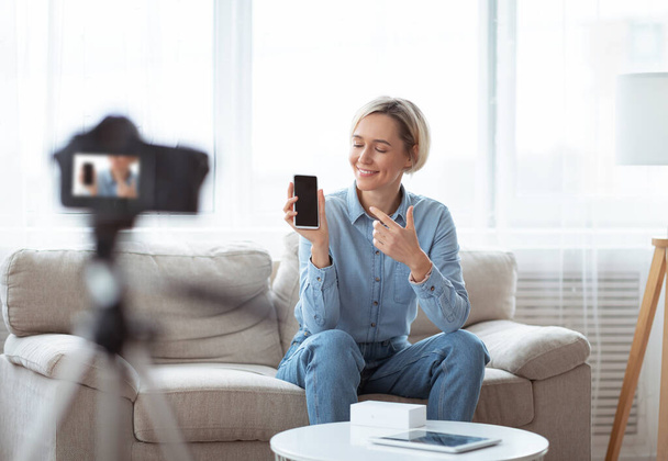 Szczęśliwy młody blogger dokonywania przeglądu wideo nowego telefonu komórkowego na profesjonalny aparat fotograficzny, filmowanie treści do jej vlog w domu - Zdjęcie, obraz