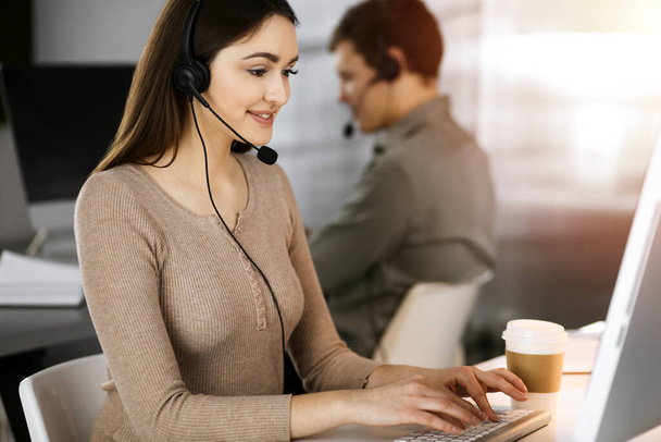 Call center operators at work. Two young people in headsets are talking to the clients, while sitting in sunny office - Foto, imagen