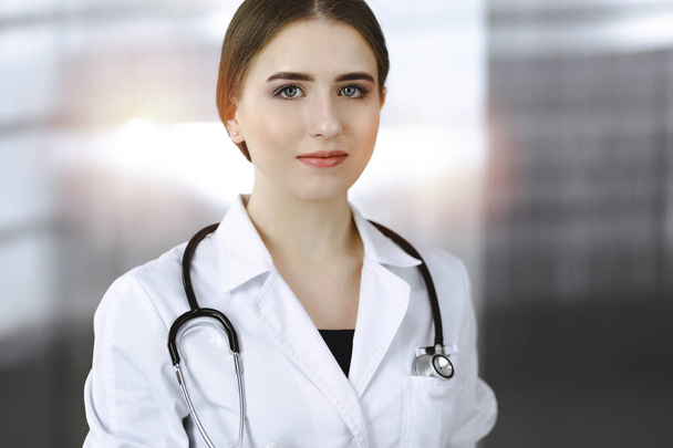 Friendly female doctor standing and holding clipboard in modern clinic. Portrait of cheerful smiling physician - Foto, afbeelding