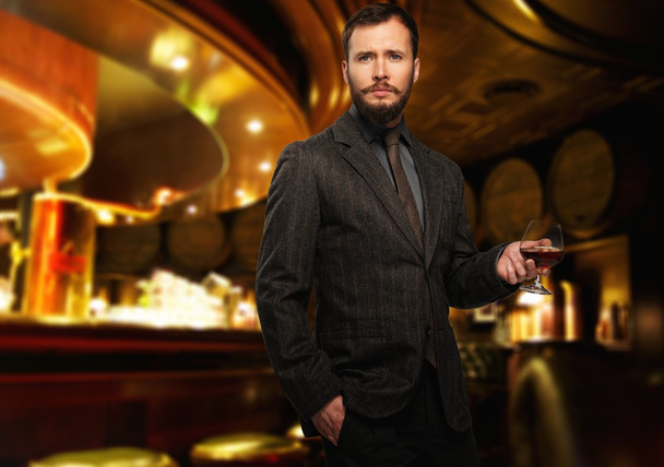 knappe goed-geklede man in jas met glas van de drank in restaurant interieur  - Foto, afbeelding