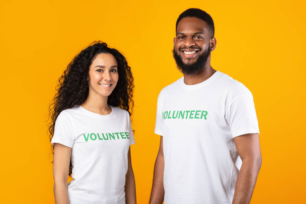 Multiraciale vrijwilligers poseren glimlachen om camera staande op gele achtergrond - Foto, afbeelding