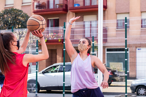 two caucasian girls play basketball with their masks on - Foto, Imagen
