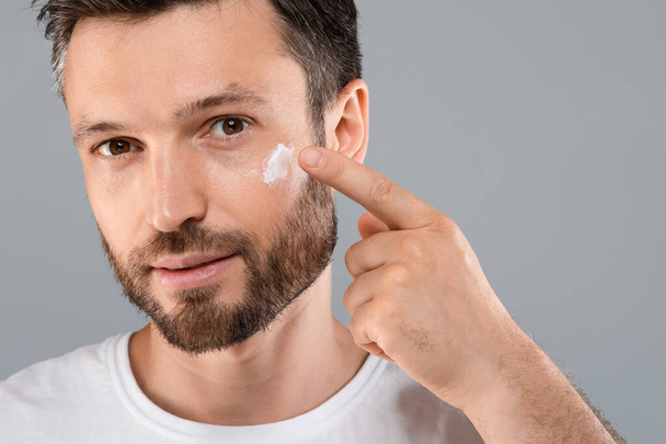 Closeup of bearded man applying face cream on grey - Zdjęcie, obraz