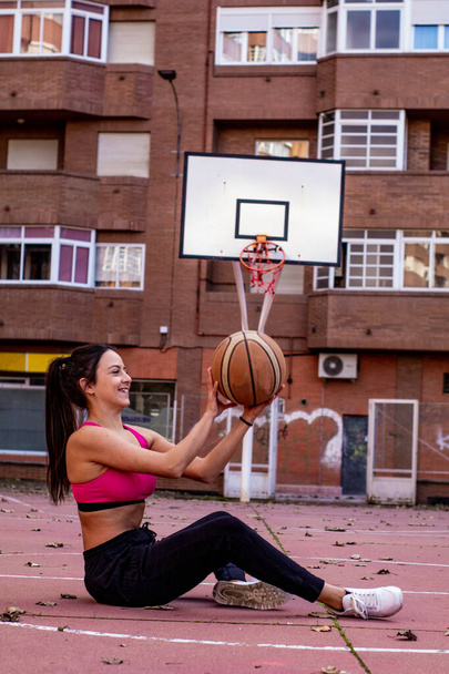 un jugador de baloncesto en ropa deportiva está acostado en medio de una cancha de baloncesto mientras juega con la pelota - Foto, imagen