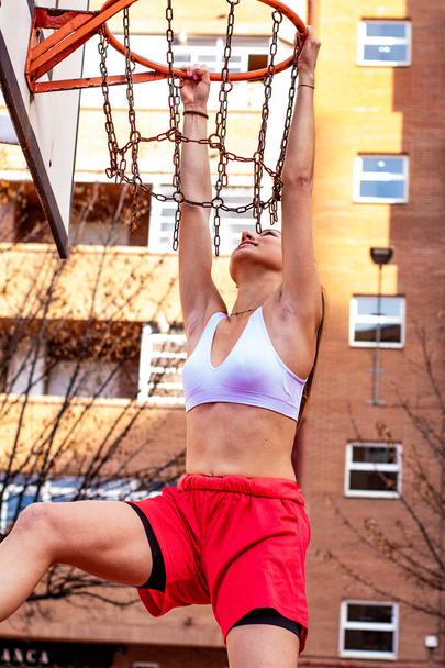 A blonde girl basketball player grabs the basketball hoop - Fotoğraf, Görsel