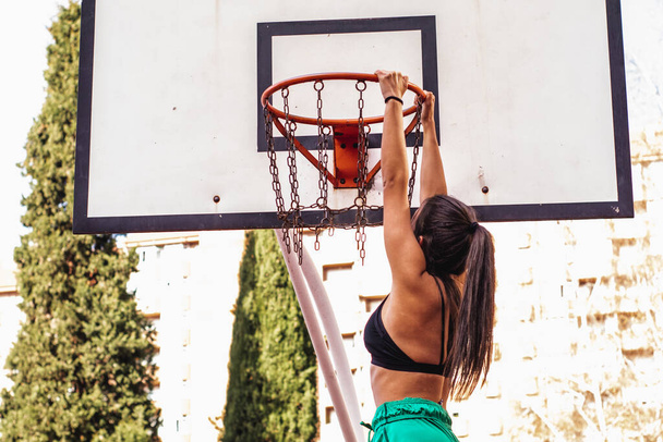 Una jugadora de baloncesto caucásica de cabello castaño se cuelga del aro de baloncesto - Foto, imagen