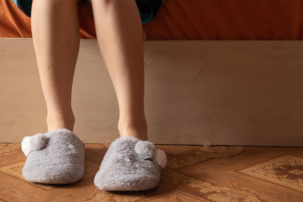 vrouwelijke voeten in huis grijze slippers op de koude vloer thuis - Foto, afbeelding