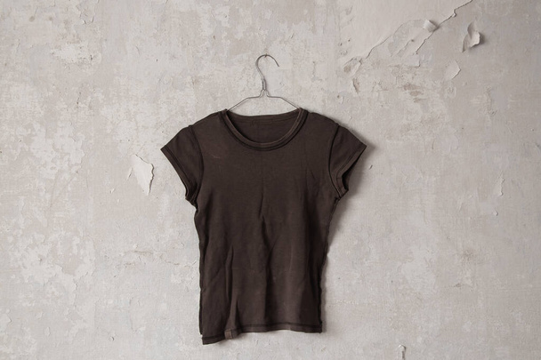 hnědé ženské tričko pověšené na ramínku na staré špinavé bílé stěně doma - Fotografie, Obrázek