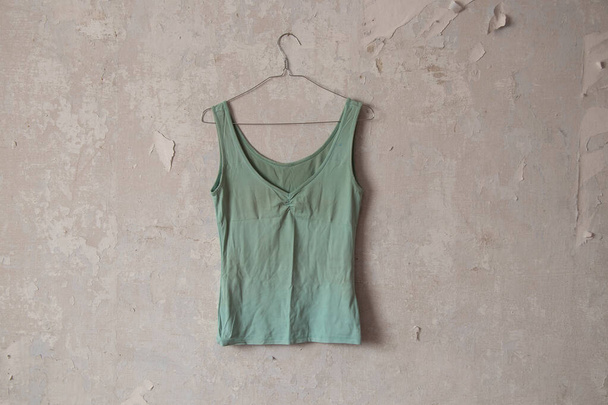 vihreä t-paita roikkuu henkarissa vanhassa likaisessa valkoisessa seinässä kotona - Valokuva, kuva