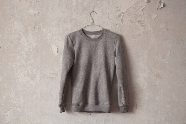 gray warm jacket hanging on a hanger on the old dirty white wall of the house - Photo, Image