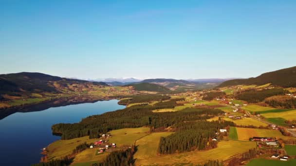 Schöne nordische Kulturlandschaft mit klarem blauen See, grünen Feldern und Bauernhäusern und schneebedeckten Bergen in der Ferne. - Filmmaterial, Video