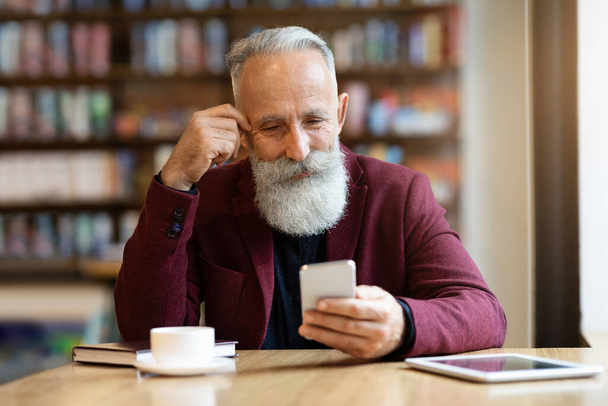 Älterer grauhaariger Mann trinkt mit Smartphone Kaffee im Café - Foto, Bild