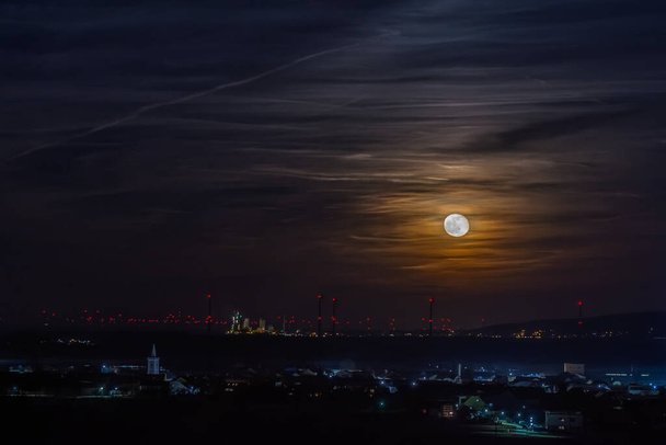 shining moon on the sky with clouds and illuminated city in the night - Photo, Image