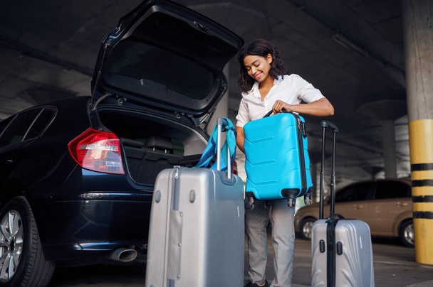 Happy woman with many suitcases in car parking. Female traveler with luggage in vehicle park lot, passenger with bag. Girl with baggage near automobile - Photo, image