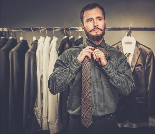 Handsome man with beard tying a tie in a clothing store - Photo, Image