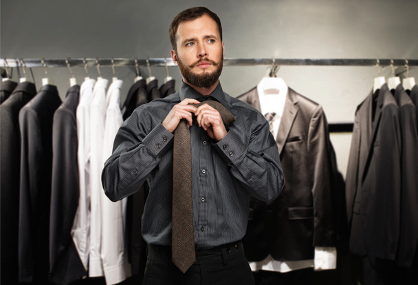 Красивий чоловік з бородою зав'язує краватку в магазині одягу
 - Фото, зображення