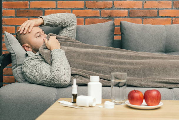 Kranker Mann auf dem Sofa hat Symptome einer Infektion Coronavirus, Covid-19 oder Grippe, Kerl ist krank und fühlt sich schwer krank. - Foto, Bild