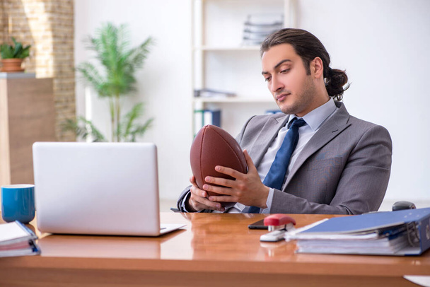 Jeune employé masculin avec ballon de rugby au bureau - Photo, image